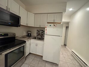 A kitchen with white cabinets, a microwave, a coffee maker, a refrigerator, and a stove.