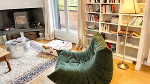Een knusse woonkamer met een groene relaxstoel, een boekenkast, een open haard en een groot raam.