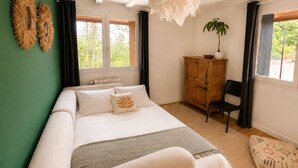 Een slaapkamer met een bed, een houten kast, een stoel, een hanglamp en een raam met gordijnen.