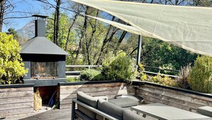 Een houten terras met een ingebouwde barbecue, buitenmeubels en een pergola voor beschutting.