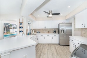 A modern kitchen with white cabinets, a stainless steel refrigerator, and a ceiling fan. - Beachside Getaway Minutes from the Gulf - Heated Pool - Sleeps 8 (Englewood)
