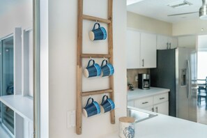 A kitchen with white cabinets, a wooden ladder shelf holding blue mugs, and a coffee maker on the counter. - Beachside Getaway Minutes from the Gulf - Heated Pool - Sleeps 8 (Englewood)
