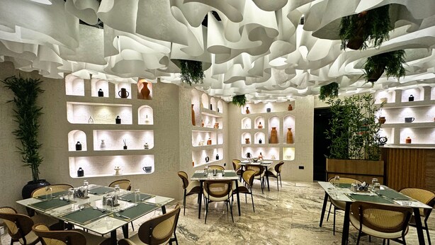 A restaurant with marble flooring, wicker chairs, and a ceiling with unique, abstract designs. - Amazonia Luxury  (Abuja)