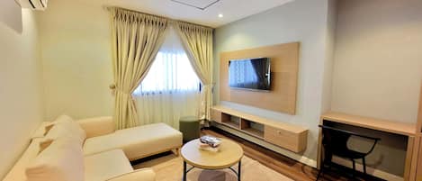 A modern living room with a sofa, a coffee table, a TV mounted on the wall, and a desk area.
