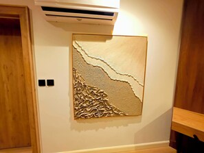 A room with a textured wall art piece, a wooden door, and a white air conditioning unit. - Amazonia Luxury  (Abuja)