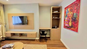 A modern hotel room with a flat-screen TV, a desk with a chair, a bookshelf, and a large abstract painting on the wall. - Amazonia Luxury  (Abuja)