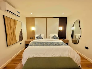 A hotel room with a large bed, bedside tables, a wall-mounted mirror, and a wall-mounted air conditioner. - Amazonia Luxury  (Abuja)