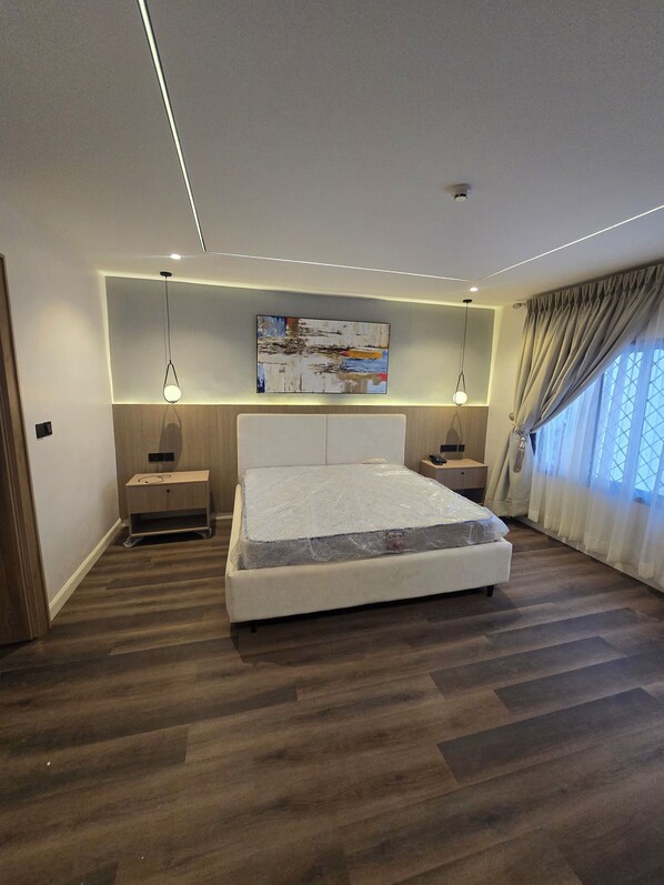 A modern bedroom with a large bed, bedside tables, a ceiling light, and a painting.