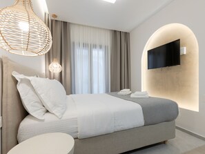 Ein modernes Hotelzimmer mit einem Bett, einem runden Tisch, einem an der Wand montierten Fernseher und einem großen Fenster mit Vorhängen.
