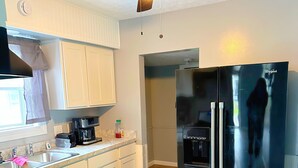 Une cuisine équipée d’une cuisinière à gaz, d’un réfrigérateur, d’un ventilateur de plafond et d’une fenêtre avec des rideaux.