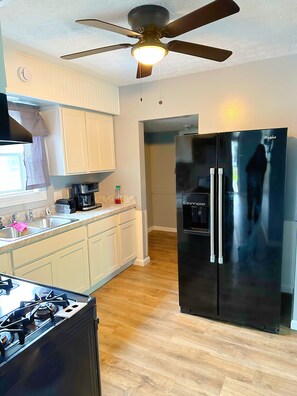A kitchen with a gas stove, a refrigerator, a ceiling fan, and a window with curtains. - Home away from home (Akron)
