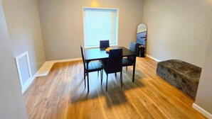 Un coin repas avec une table et des chaises, une fenêtre avec des stores et un luminaire au plafond.