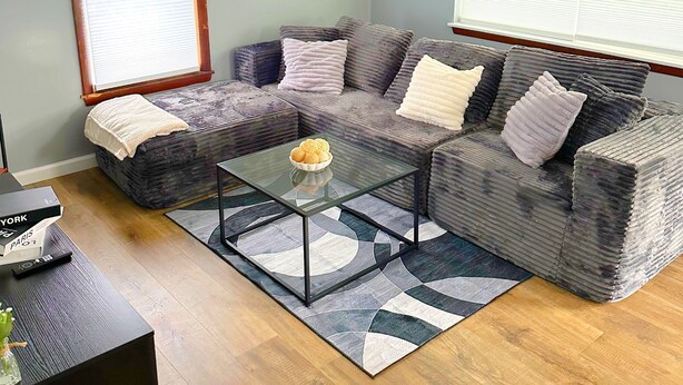 Un salon avec un canapé d’angle, une table basse en verre et un tapis.