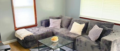 A living room with a sectional sofa, a glass coffee table, and a rug.