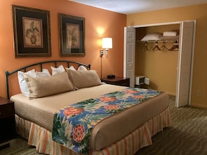 A hotel room with a bed, a nightstand, a lamp, a closet, and two framed pictures on the wall.