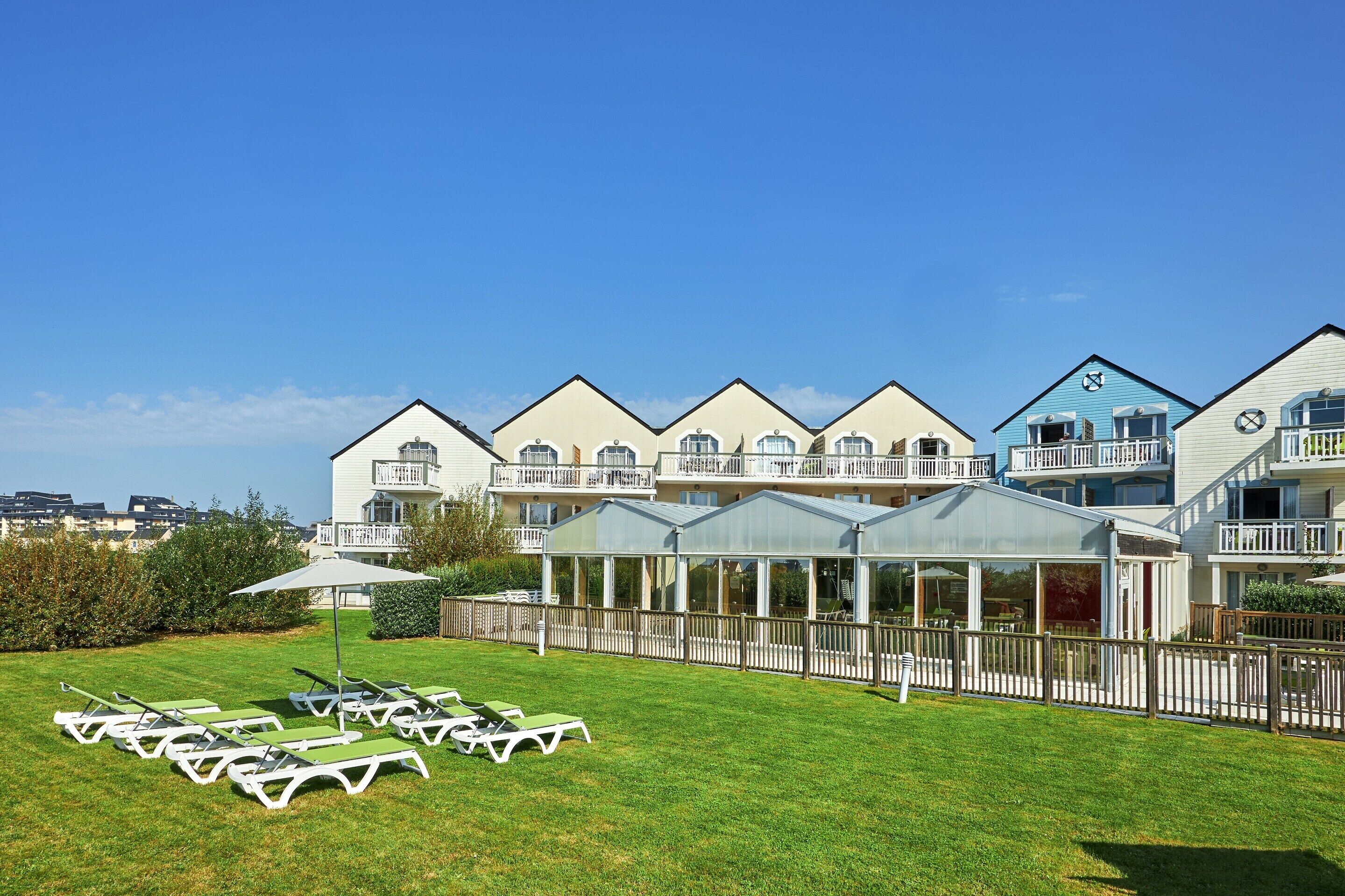 A hotel with multiple balconies, a covered outdoor area, and a lawn with sun loungers.