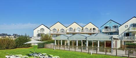 A hotel with multiple balconies, a covered outdoor area, and a lawn with sun loungers.