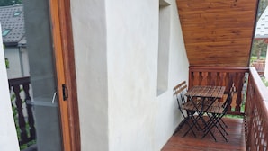 A wooden deck with a table and chairs, a glass door, and a white wall. - 1st-floor apartment+2 private parking spaces.large, peaceful balcony. (Le Monêtier-les-Bains)