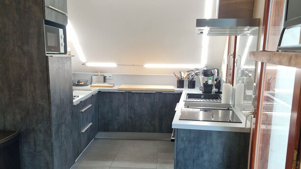 A modern kitchen with a microwave, stove, and sink. There is a dining table with chairs. - 1st-floor apartment+2 private parking spaces.large, peaceful balcony. (Le Monêtier-les-Bains)