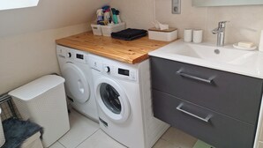 A compact laundry room with a washing machine, a drying rack, a wooden countertop, a sink with a mirror, and a trash bin. - 1st-floor apartment+2 private parking spaces.large, peaceful balcony. (Le Monêtier-les-Bains)