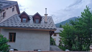 A building with a sloped roof, a chimney, and a wooden fence in the foreground. - 1st-floor apartment+2 private parking spaces.large, peaceful balcony. (Le Monêtier-les-Bains)