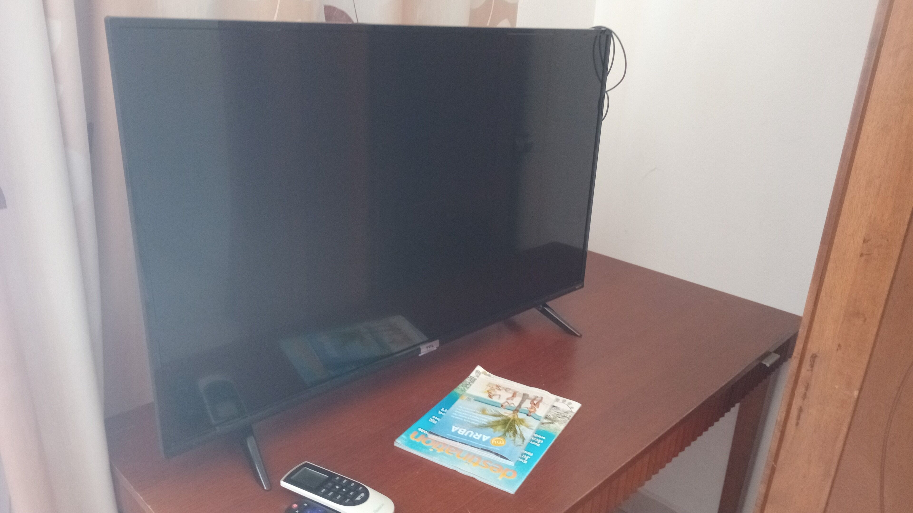 Television on puisen jalustan päällä, kaukosäädin ja lehti jalustan päällä.