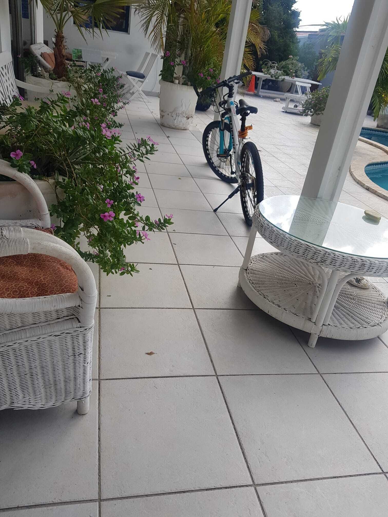 Un espacio al aire libre con techo, mobiliario de mimbre, una bicicleta y una piscina al fondo.