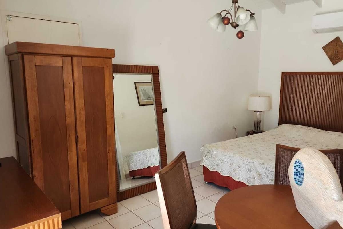 Een slaapkamer met een houten garderobe, een bed met een geborduurde spreideken, een stoel, een tafel en een bedlamp.