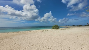 Una playa arenosa con agua turquesa cristalina y nubes dispersas.