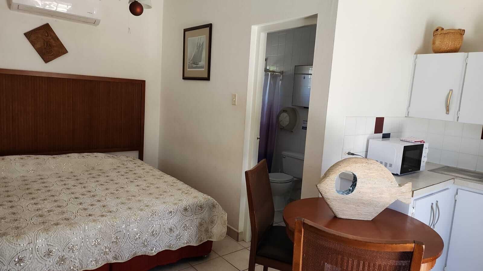 Ein Schlafzimmer mit einem Bett, einem hölzernen Kopfteil, einem kleinen Tisch mit einem Korbstuhl, einer Mikrowelle und einem Schrank.