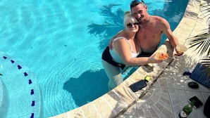Una piscina con borde de azulejos, un teléfono inteligente, una tableta y una botella al borde de la piscina.