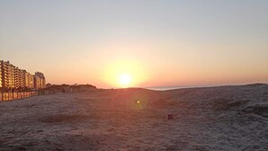 Una playa con un atardecer, arena y un edificio con luces a la izquierda.