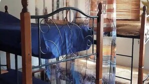 Estructura de cama metálica con colchón azul, cabecera de madera y ventana con persianas.