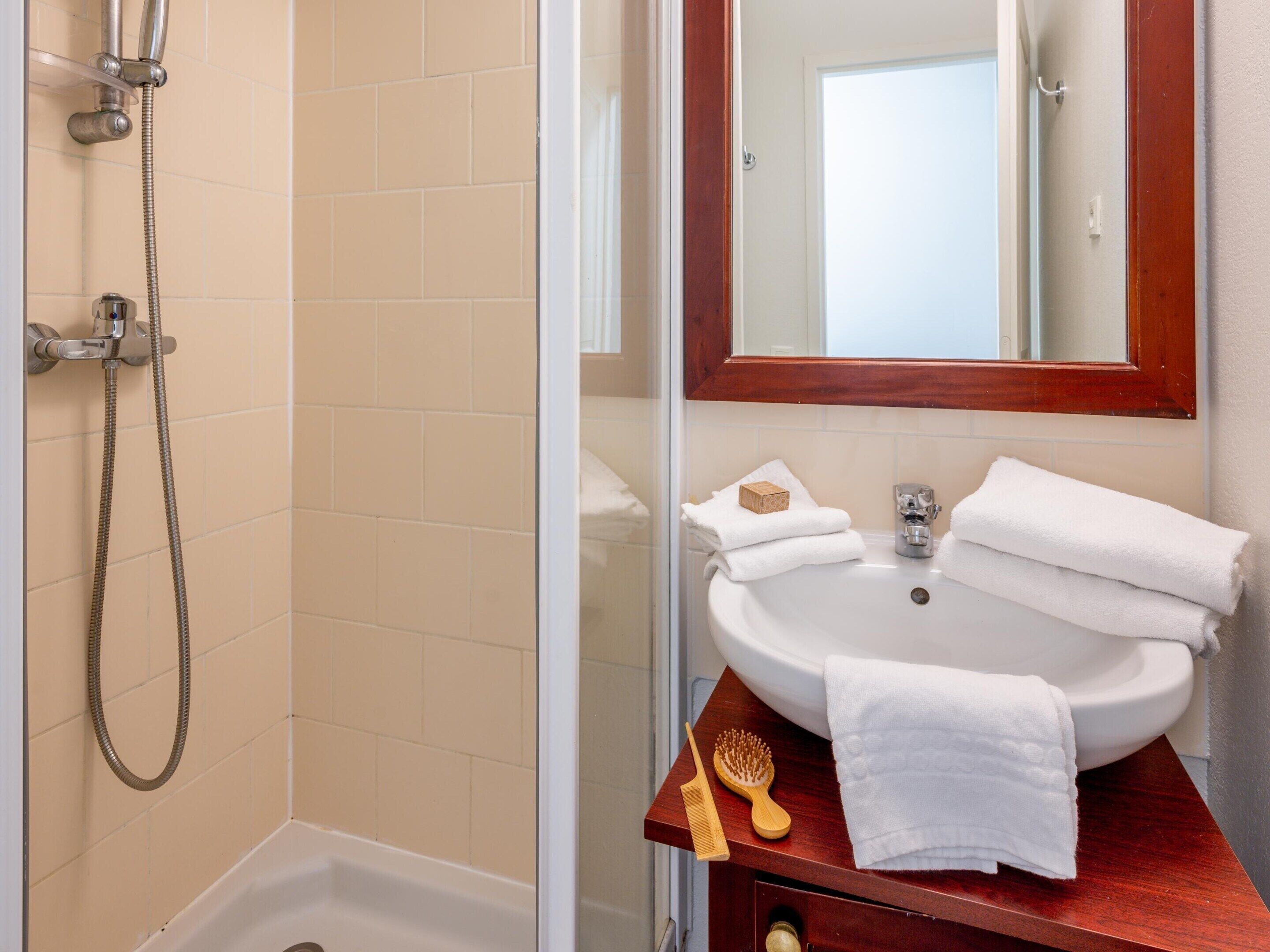 A bathroom with a glass shower enclosure, a sink with a mirror, and toiletries.