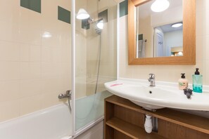 A bathroom with a shower, a sink with toiletries, and a mirror. - Branville Duplex With Garden and Pool (Branville)