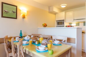 A breakfast table set with plates, cups, and a bowl of fruit, a microwave, and a sink in the background. - Branville Duplex With Garden and Pool (Branville)