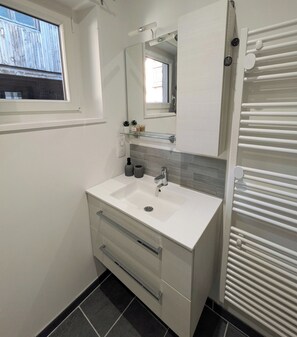 Een badkamer met een wit wastafel, een spiegel, een handdoekhouder en een raam.
