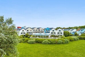 A row of modern, multi-story buildings with balconies, a covered outdoor area, and a well-maintained lawn. - Normandy Coastal Apartment for 5 (Courseulles-sur-Mer)