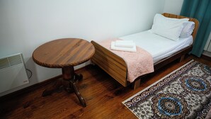 A small room with a single bed, a round wooden table, and a patterned rug. - Meiman Guest House (Karakol)