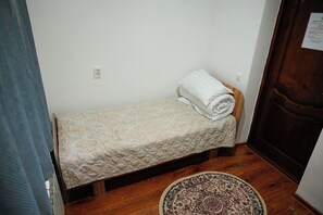 A small, single-bed room with a wooden floor, a patterned rug, and a door with a notice on it.