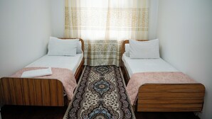 A room with two single beds, a patterned rug, and a window with a sheer curtain. - Meiman Guest House (Karakol)