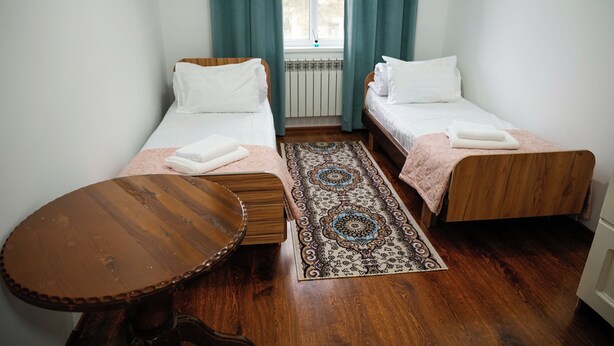 A room with two wooden beds, a round wooden table, and a patterned rug. - Meiman Guest House (Karakol)