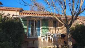Une maison avec un toit en tuiles, un patio couvert avec des chaises et une table, et un barbecue.