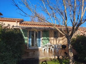 Ein Haus mit Ziegeldach, einer überdachten Terrasse mit Stühlen und Tisch sowie einem Grill.