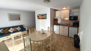 Un espace de vie compact comprenant une table à manger, des chaises, un canapé, un coin cuisine équipé d’appareils électroménagers et un tableau accroché au mur.