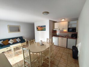 Ein kompakter Wohnbereich mit Esstisch, Stühlen, einer Couch, einer Küchenzeile mit Geräten und einem Bild an der Wand.