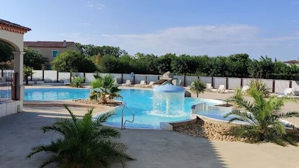 Une piscine agrémentée d’un élément décoratif aquatique, entourée de palmiers et de chaises longues.