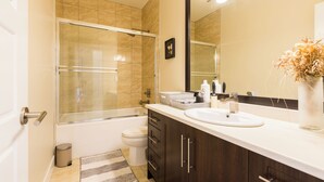 Un baño moderno con ducha envuelta en vidrio, un lavabo blanco, armarios de madera oscura y un espejo grande.