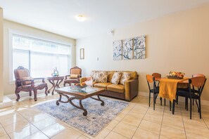 Ein Wohnzimmer mit einer Couch, Sesseln, einem Couchtisch und einem Esstisch mit Stühlen.