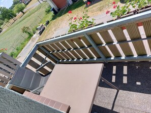 Ein überdachter Außenbereich mit Holzterrasse, einer Sitzecke mit Stühlen und Blick auf einen grünen Garten mit Pflanzen.